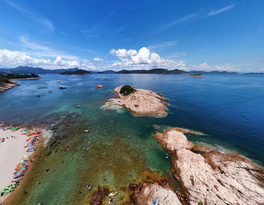 俯瞰清澈碧綠的海水、岩石島嶼和沙灘上排列整齊的彩色獨木舟,天空晴朗。