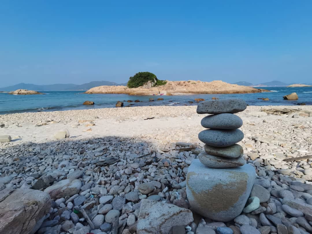 鹅卵石滩上堆叠的平衡石,背景是碧蓝大海、小岛和晴朗天空。