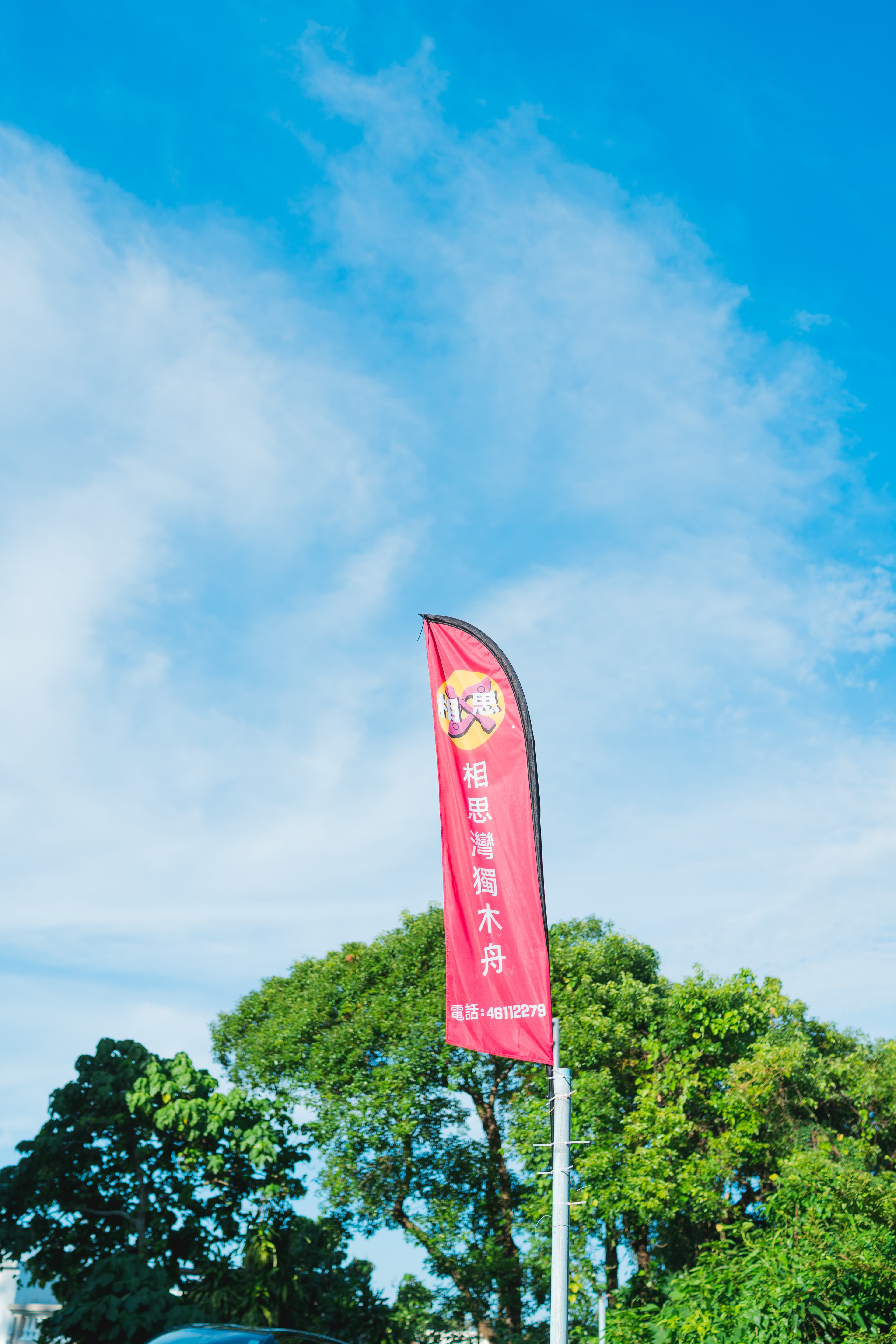 藍天綠樹背景下,一面印有「相思灣獨木舟」字樣的紅色宣傳旗幟。