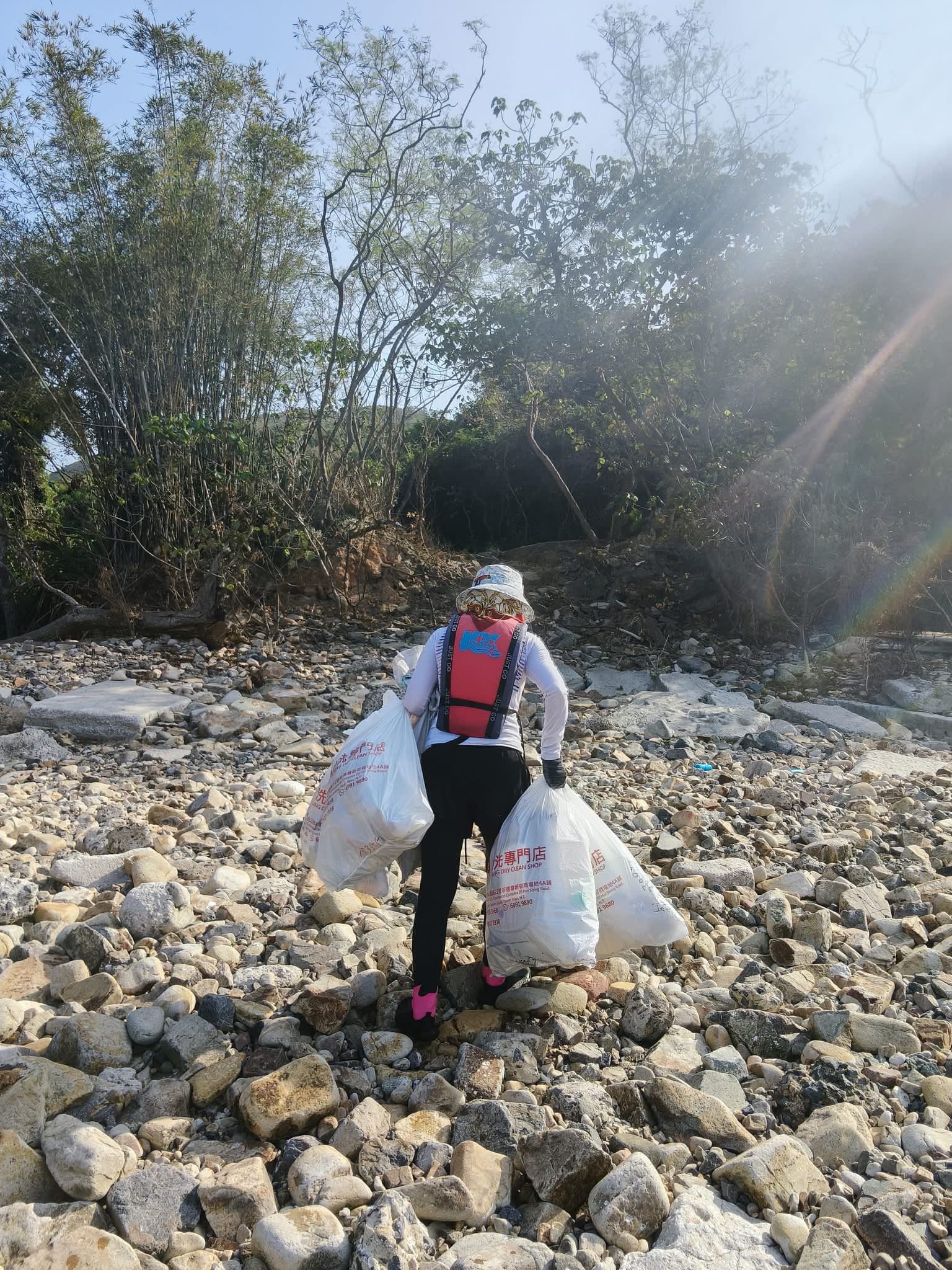 穿着救生衣的志愿者在岩石海滩上提着两大袋垃圾。